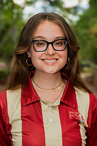 smiling female student with long, red hair and chunky black glasses