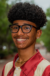 smiling male student with mid-length black fro, chunky black glasses and diamond earring studs
