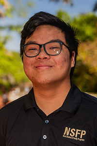 smiling male student with black hair and chunky black glasses