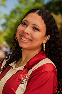 smiling female student with long brown curly hair and large gold hoop earrings