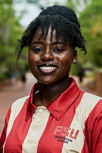 smiling female student with dark hair pulled back into a bun on the top of her head, with curly bangs