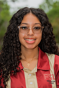 smiling female student with long curly brown hair and clear plastic rimmed glasses