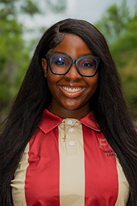 smiling female student with long wavy brown hair and oversized black-framed glasses