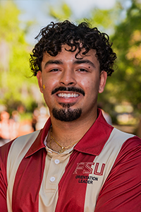 smiling male student with short dark brown curly hair, a moustache and a goatee