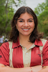 smiling female student with arms crossed and shoulder-length brown hair