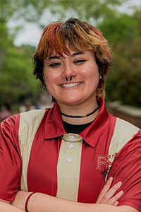 smiling student with short, colored hair with bangs. they have two nose rings and a choker on.