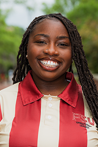 smiling female student with long brown locs and gold ball-shaped earrings