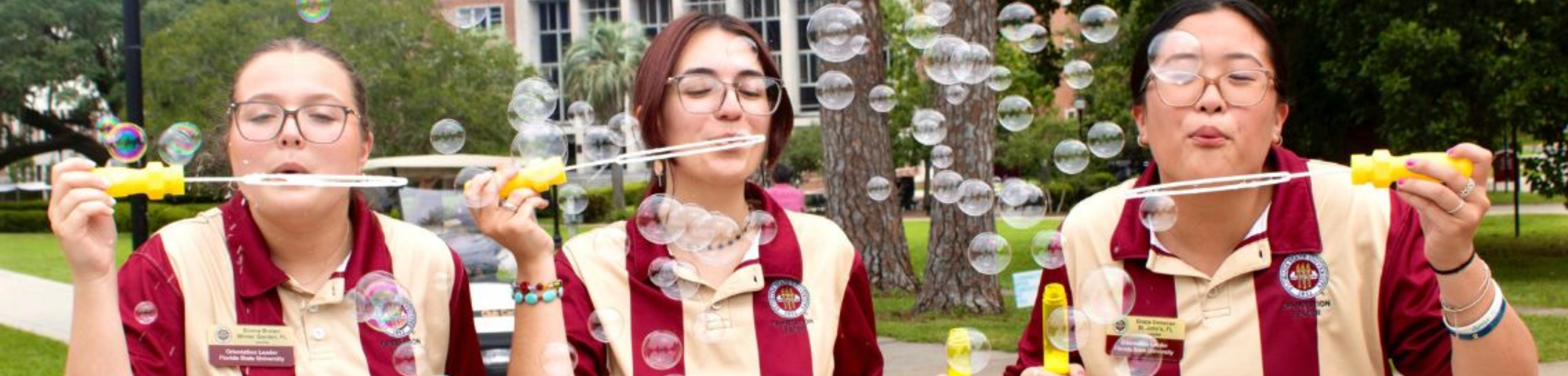 Three people wearing matching striped shirts are blowing bubbles outdoors.