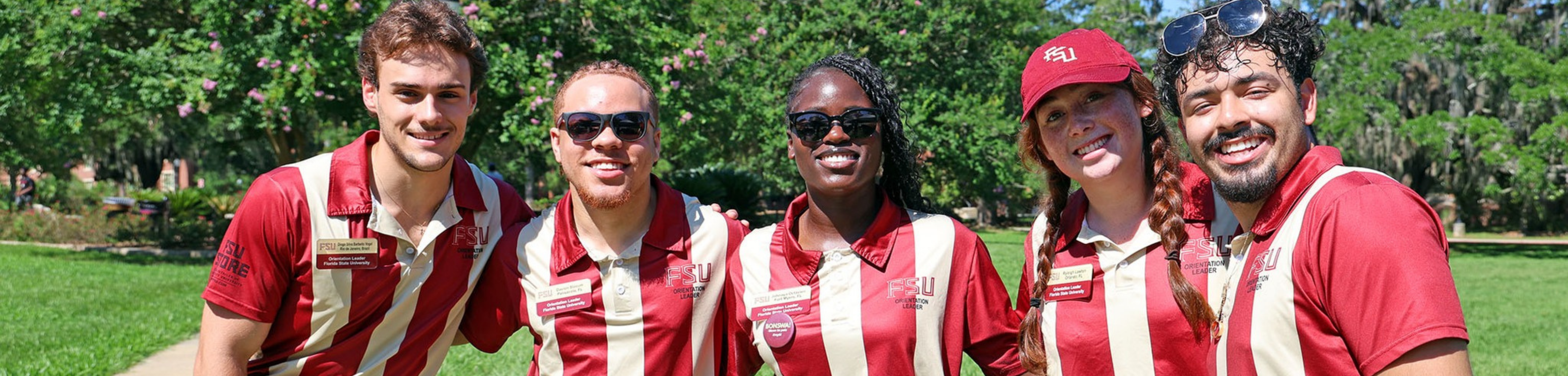 Five smiling FSU Orientation Leaders wearing garnet and gold striped polos pose together outside on a sunny day.