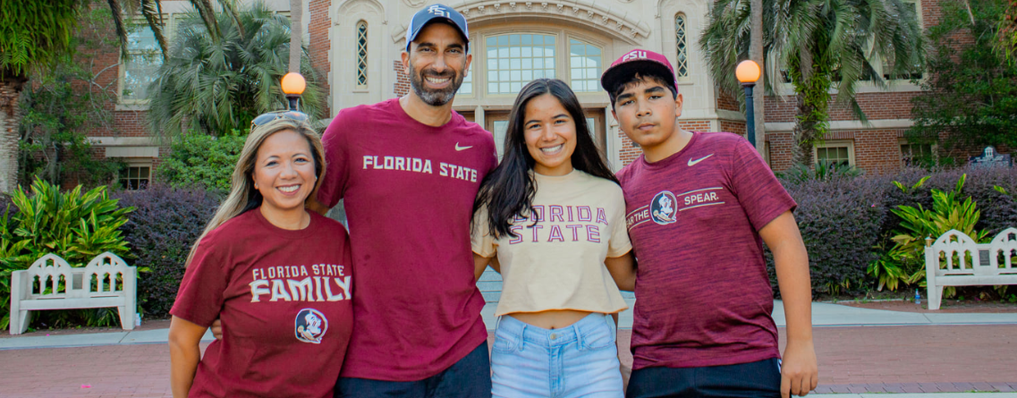 A family of four wearing Florida State University apparel poses happily in front of a campus building.
