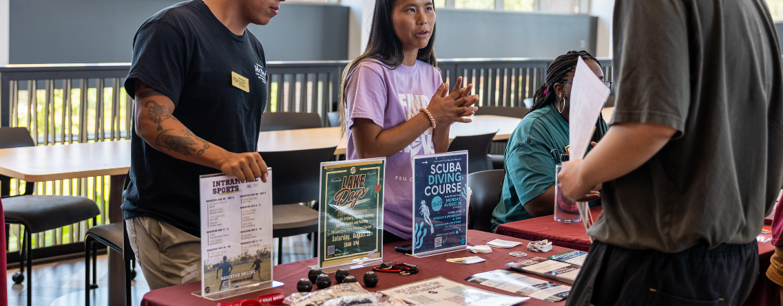 People are interacting at a table with various informational posters and items on display.