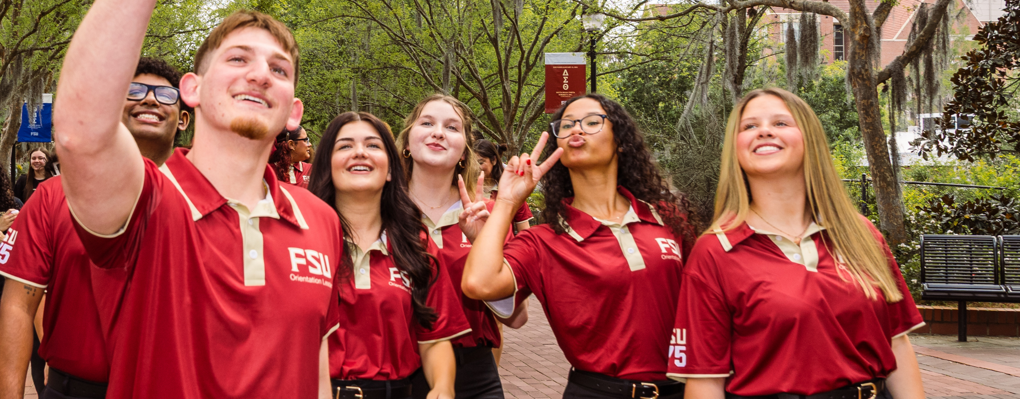 A group of six smiling Florida State University Orientation Leaders are walking together outdoors on a brick pathway.
