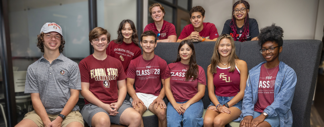 A group of students wearing Florida State University apparel is smiling and posing for a photo indoors.